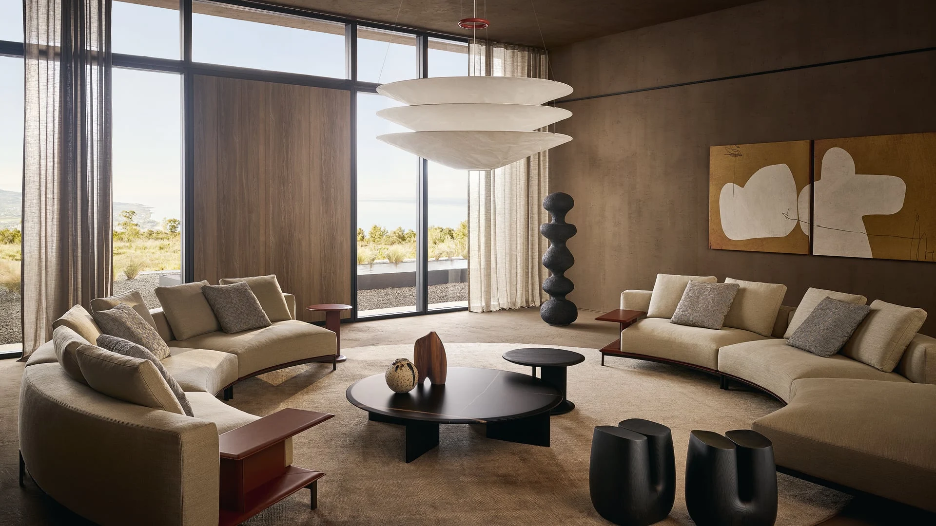 Living contemporaneo con divani curvi, una grande sospensione e opere d’arte, aperto sul paesaggio
