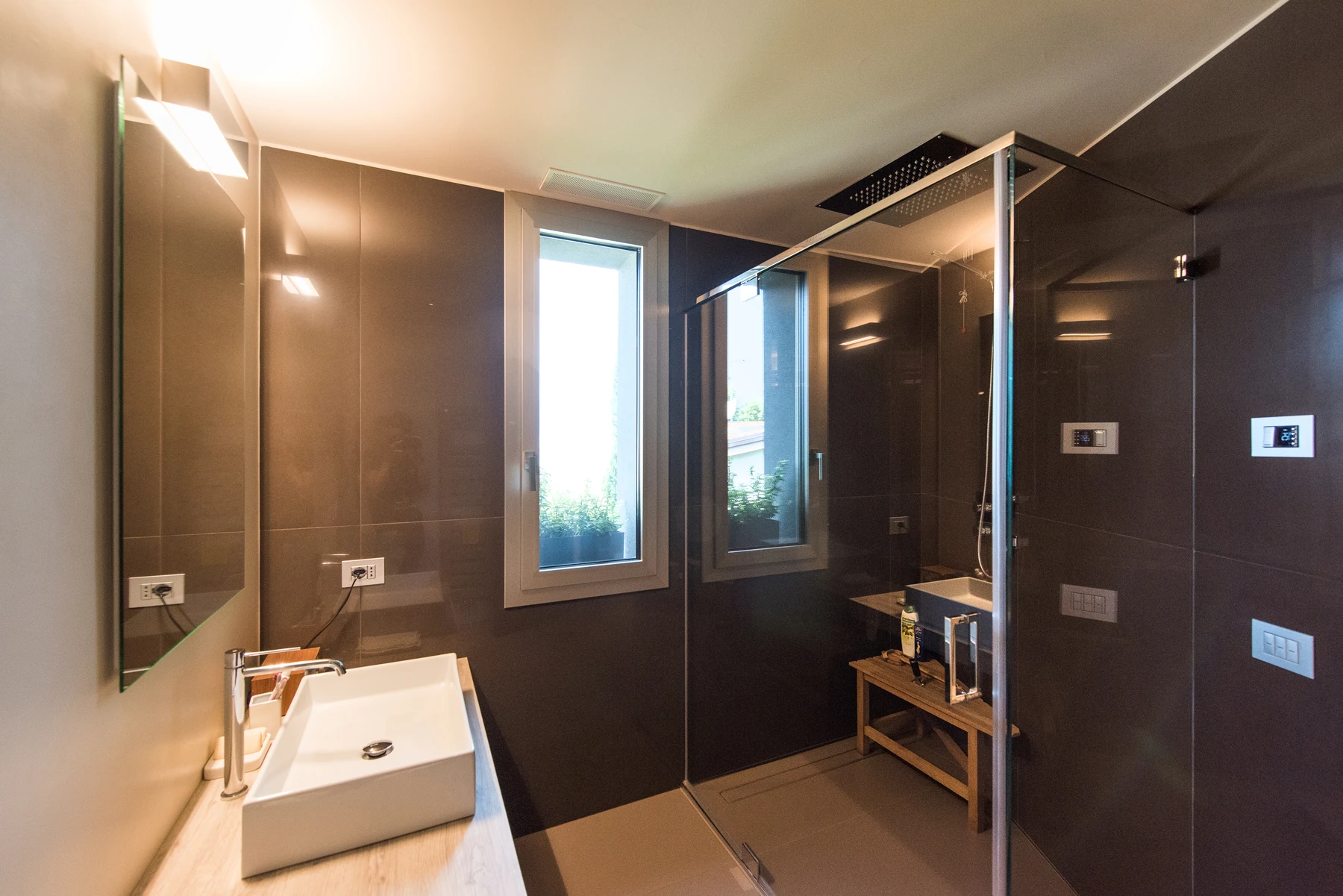 Bagno con grande doccia in vetro, soffione a pioggia a soffitto e lavabo rettangolare su piano in legno