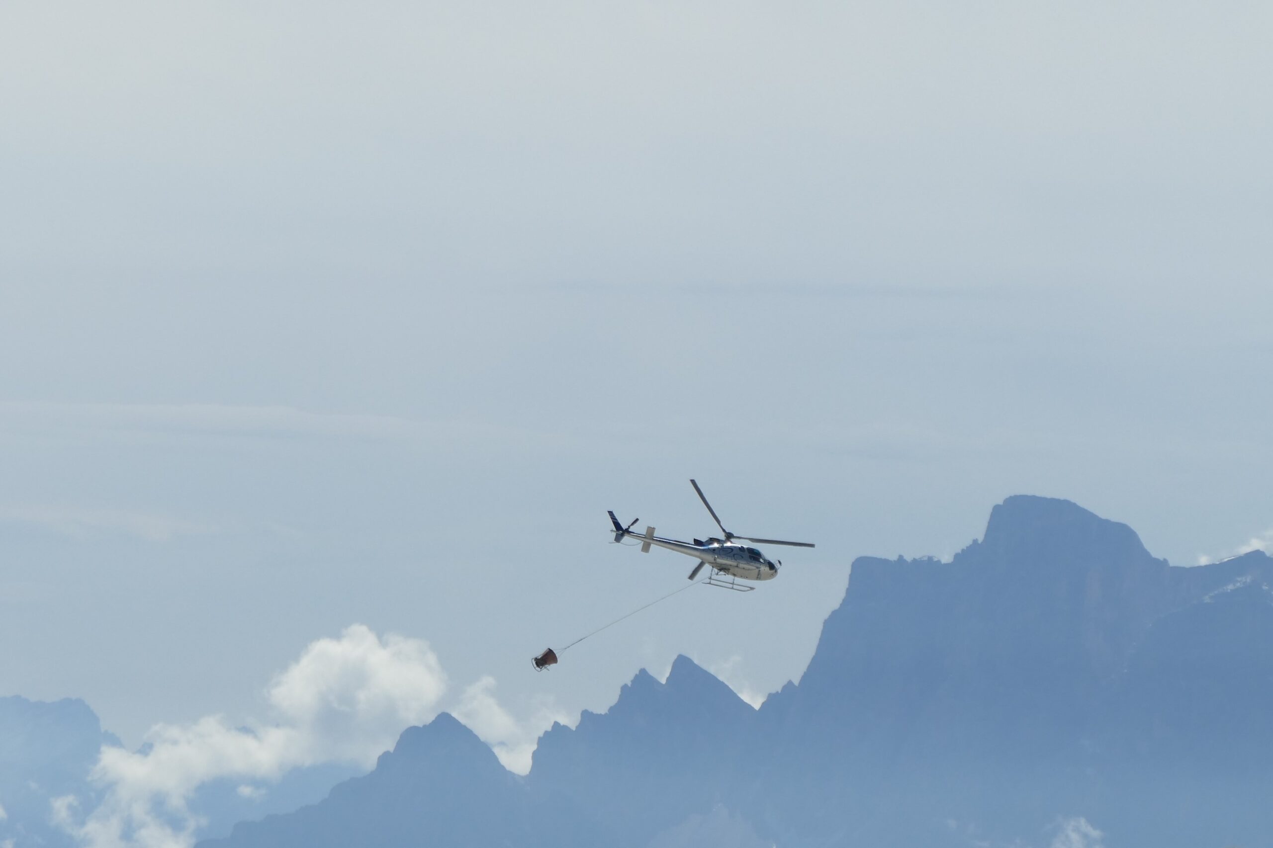 Elicottero con carico sospeso davanti alle cime delle Dolomiti